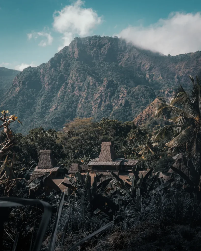 Breathtaking view of mountains, wooden huts, and lush greenery under a bright blue sky with white clouds.