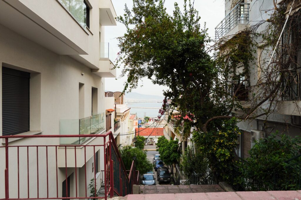 Charming urban residential street with lush greenery and a distant view of the sea on a bright day.