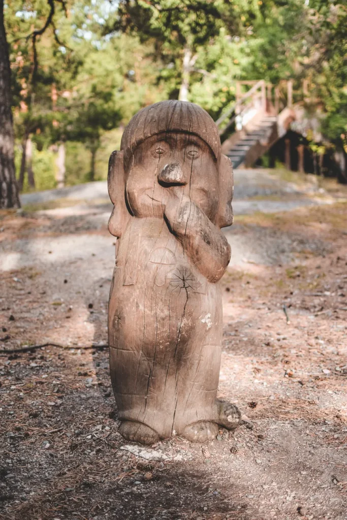 Charming wooden troll sculpture in a sunlit Swedish forest path.
