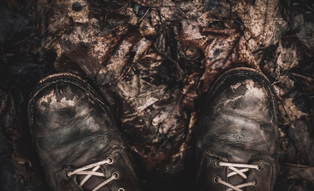 Close-up of worn leather boots on fallen autumn leaves, highlighting outdoor exploration.