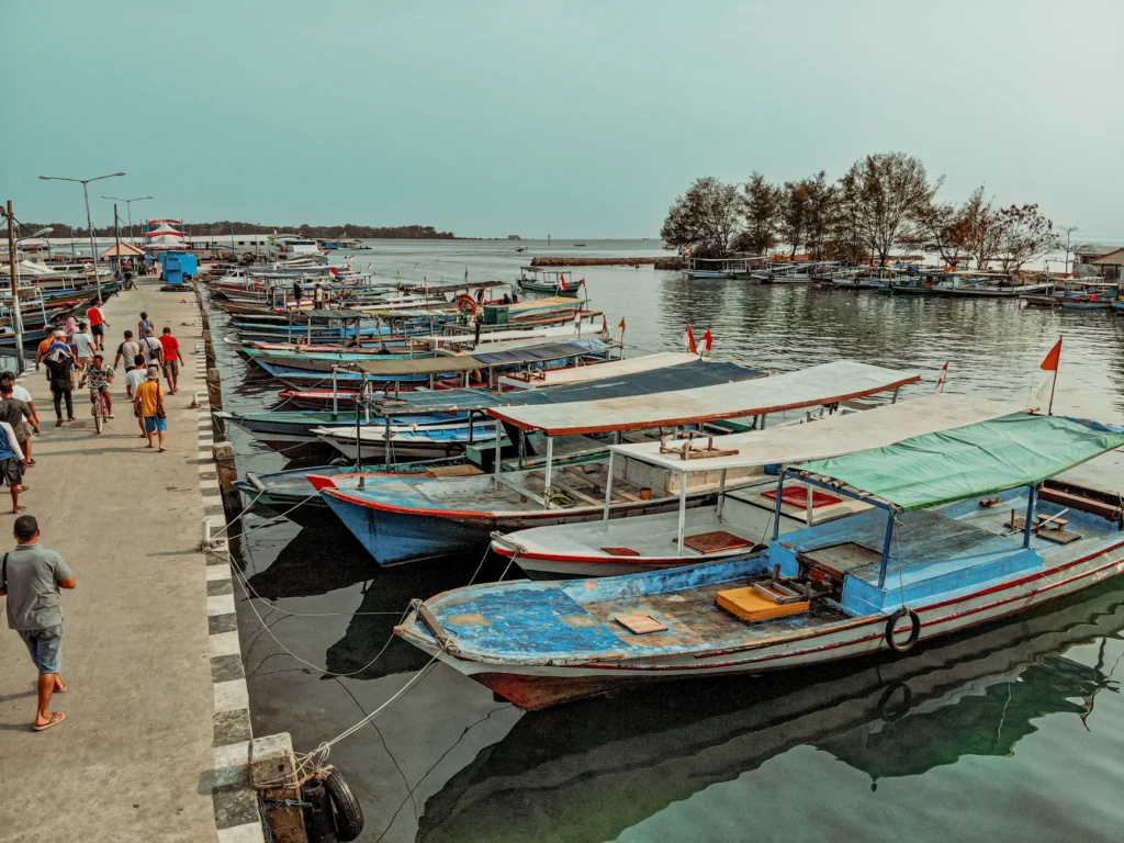 Colorful fishing boats docked at a bustling harbor in Bali, Indonesia with people walking along the pier.