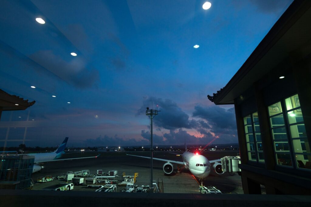Contemporary airplanes with red beacon parked on airfield near airport service vehicles and terminal at night