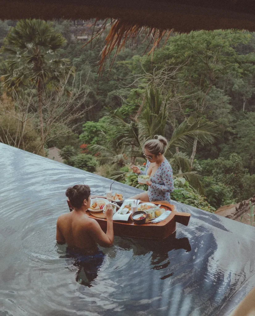 Couple enjoying breakfast on a floating tray in an infinity pool with lush greenery in Bali.