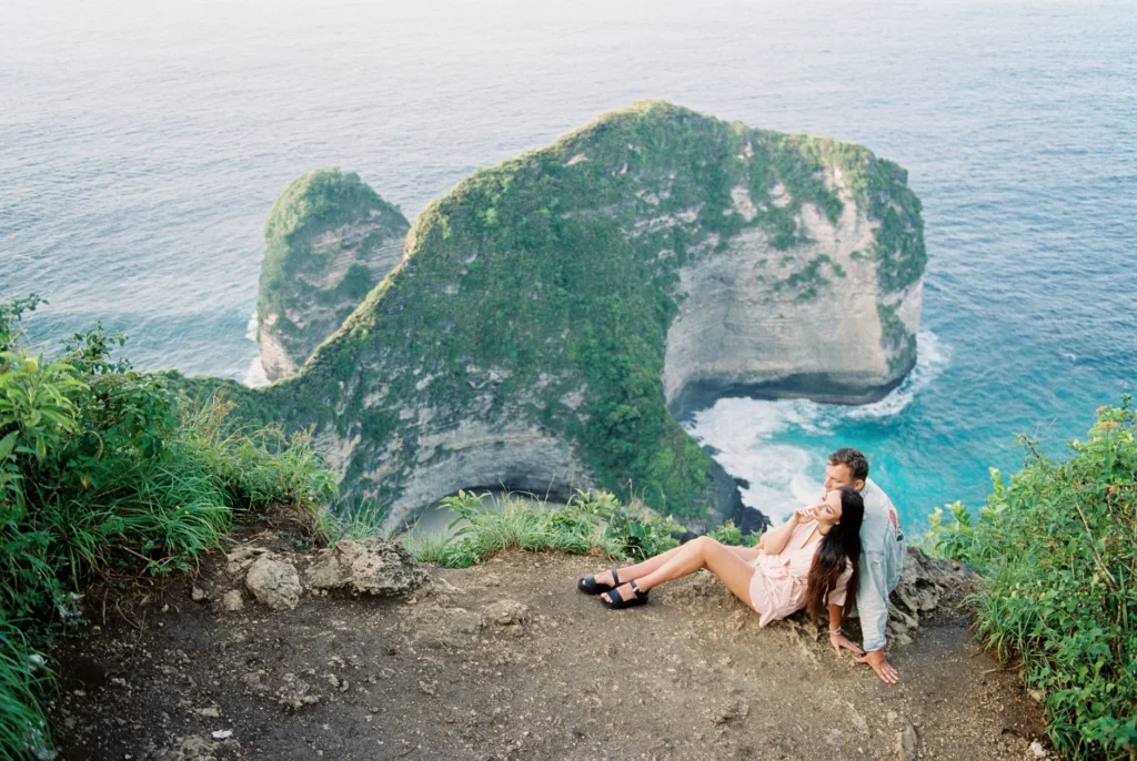Couple sitting on edge overlooking Nusa Penida cliff, Bali, Indonesia.