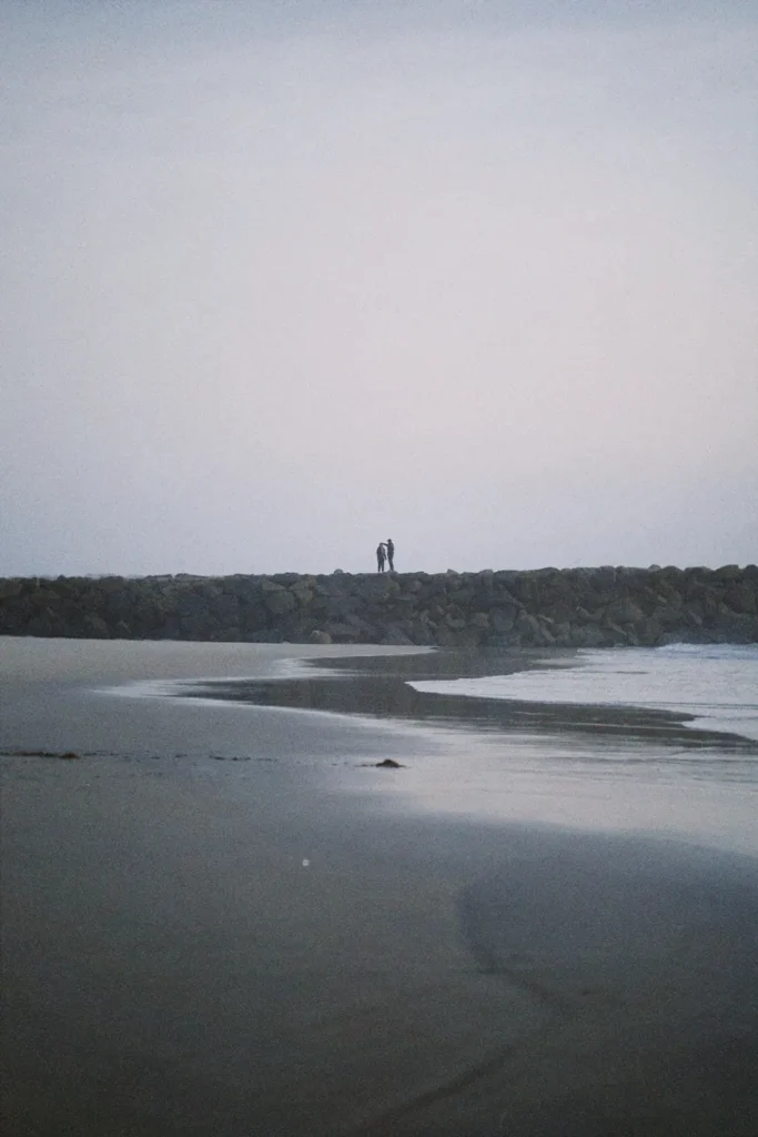 Couple walking on beach at dawn with tranquil sea and sky.