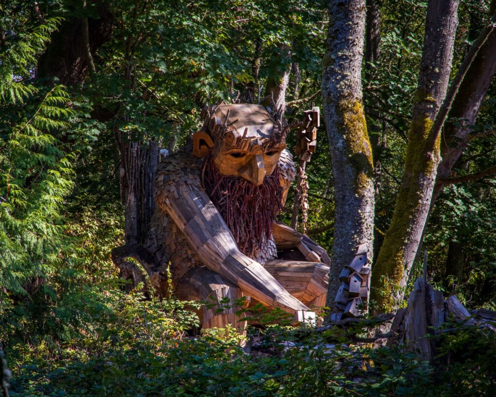 Discover a large wooden troll sculpture nestled in Vashon's lush greenery, a whimsical forest art piece.