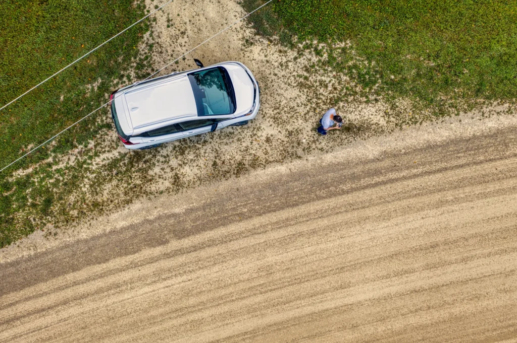 Drone shot of a car parked on a gravel road in rural Minnesota with a person nearby.