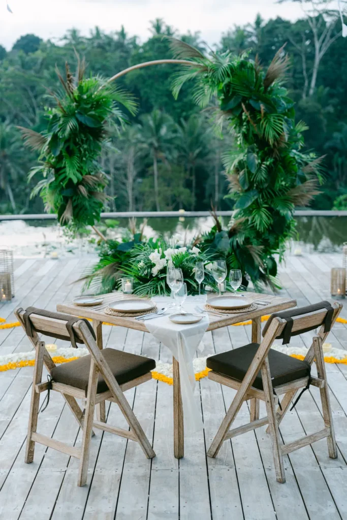 Elegant dinner setup outdoors with lush greenery and wooden chairs, perfect for romantic occasions.