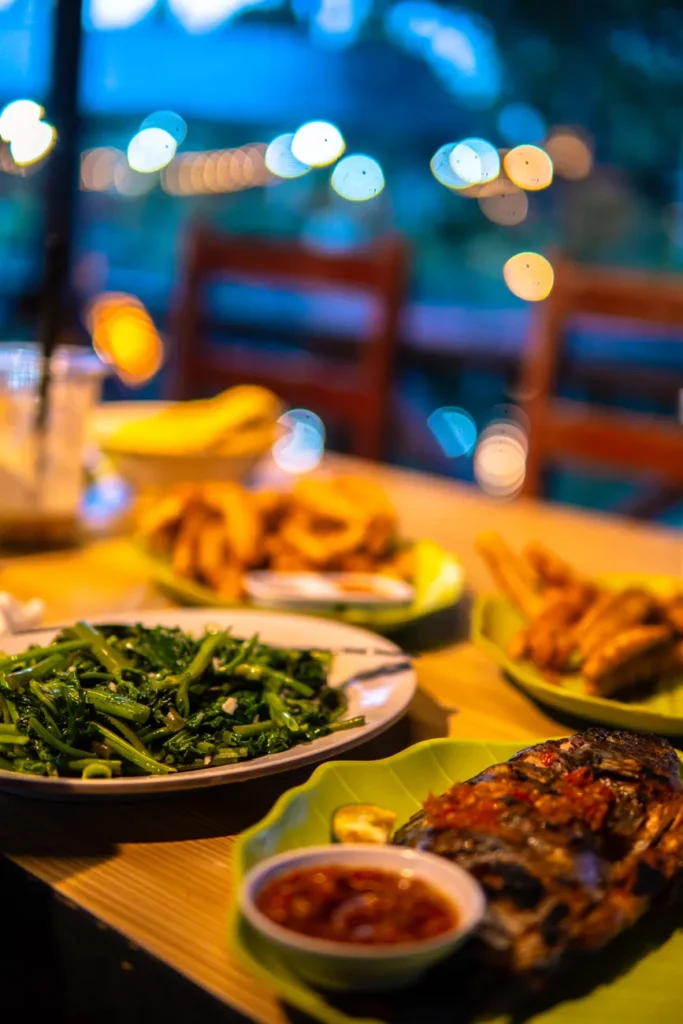 Elegant dinner table with grilled fish, leafy greens, and fried dishes, set in a warm evening ambiance.