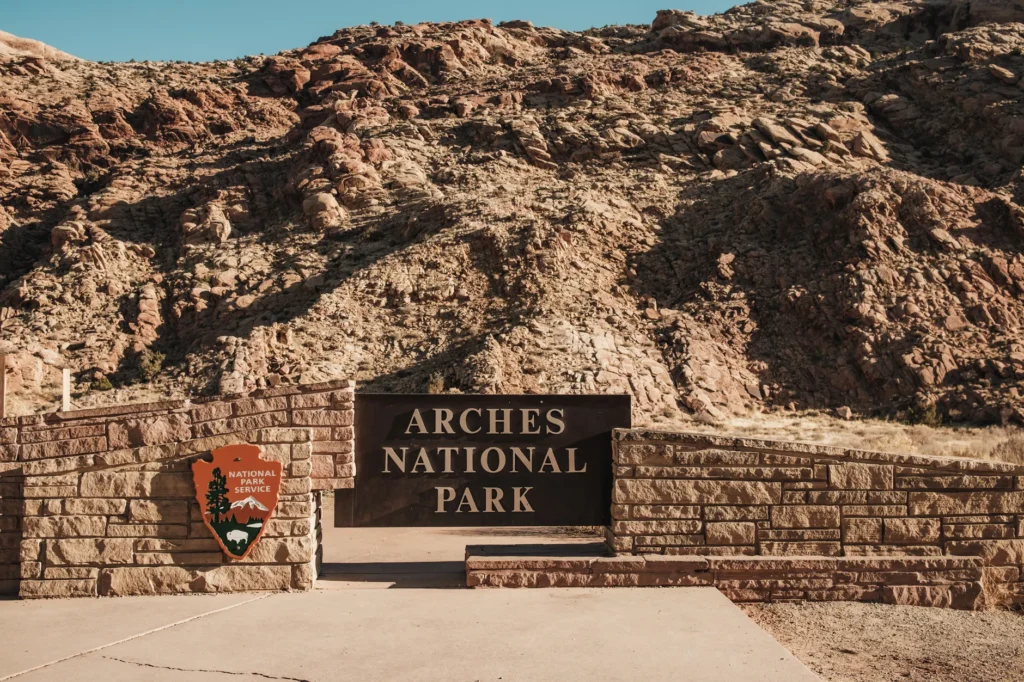 Entrance sign of Arches National Park with rocky hillside backdrop in Utah, USA.