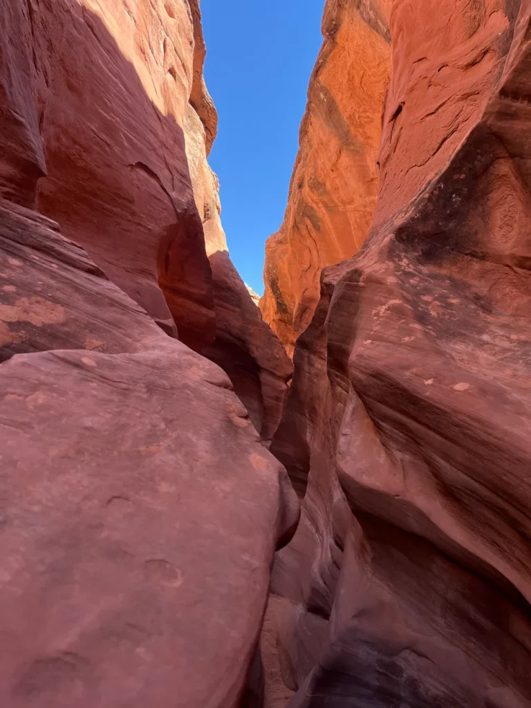 Experience the vibrant red hues and striking formations of a slot canyon, set against a clear blue sky.