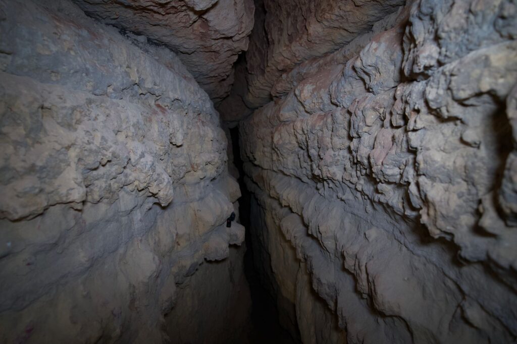 Explore a narrow and rough stone cave passage in Winslow, AZ, illuminated by natural light.