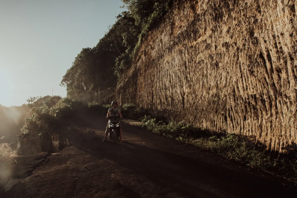 Explore Bali's rugged landscapes on a motor scooter along a dirt road at sunset.