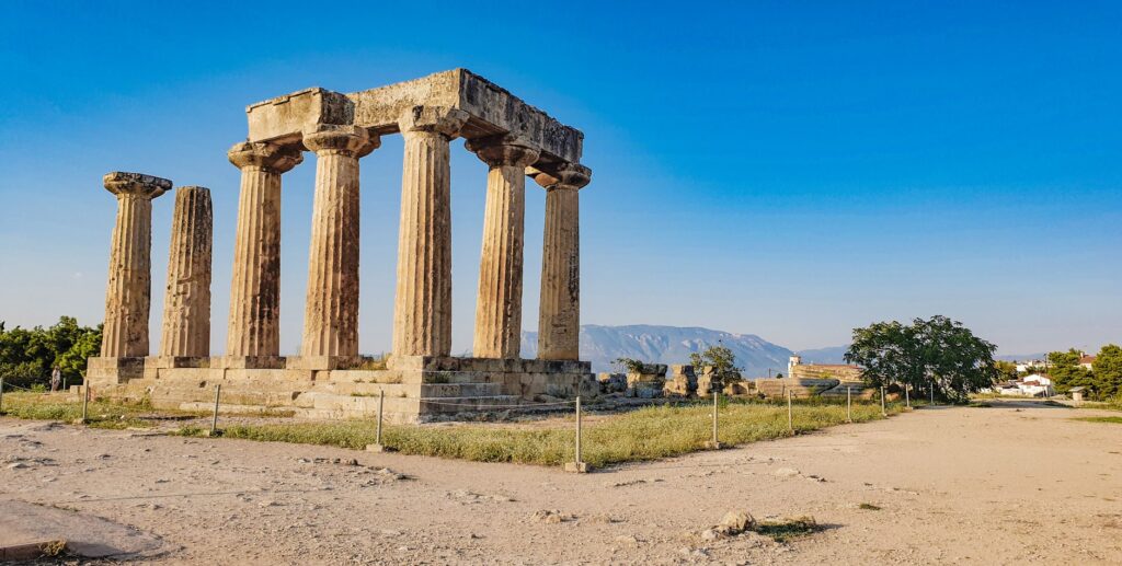 Explore the ancient ruins of the Temple of Apollo in Corinth, Greece, bathed in sunlight.