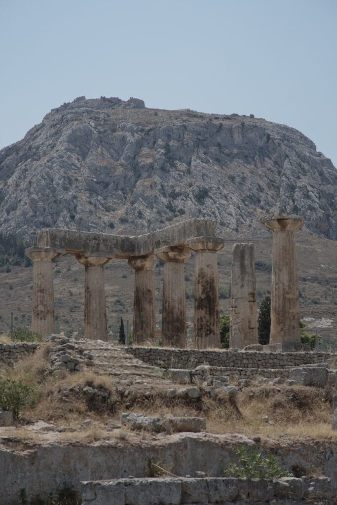 Explore the historic Temple of Apollo against a scenic mountainous backdrop in ancient Corinth.