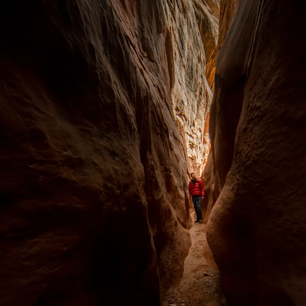 Explore the majestic narrow slot canyon in Utah with a lone hiker in a vibrant red jacket.