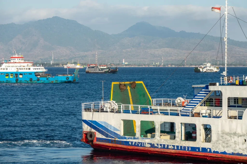 Ferry boats in a calm harbor with a mountainous backdrop on a sunny day.
