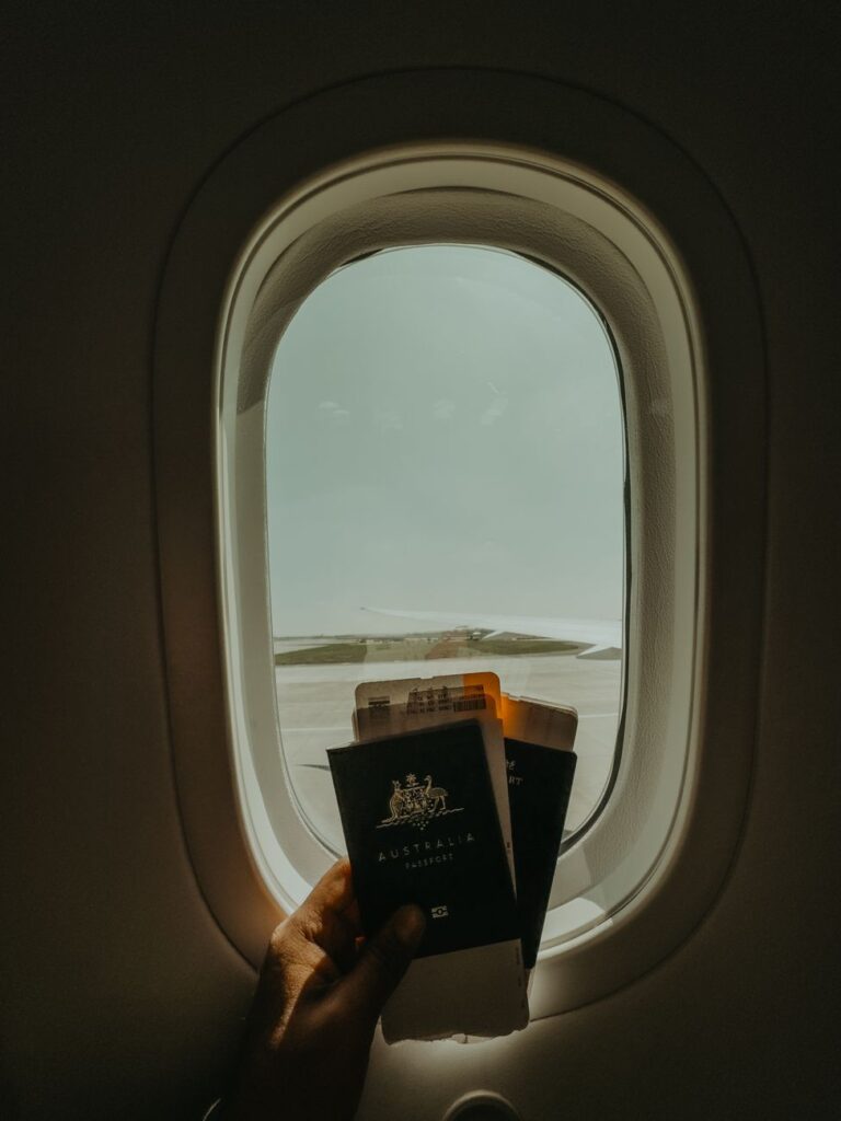 Hand holding passport and tickets by airplane window, preparing for travel adventure.