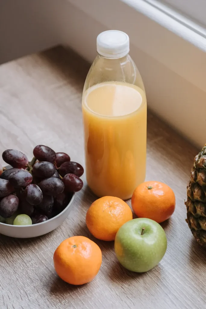 High angle of plastic bottle with juice bowl with red grapes and some mandarins and green apple on table