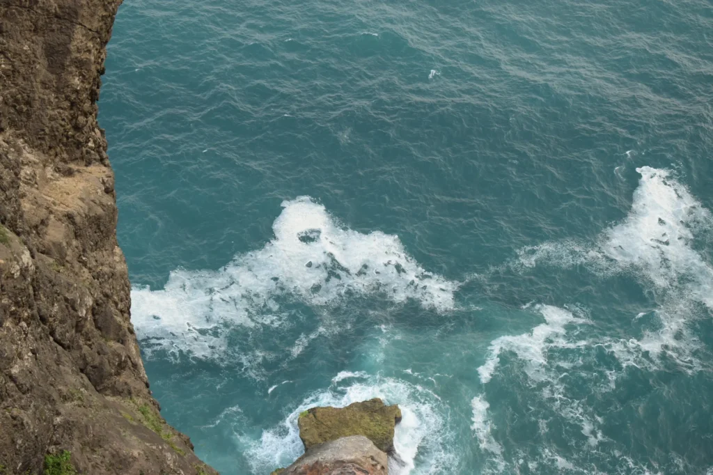 High-angle shot of ocean waves crashing against rocky cliffs, showcasing a dramatic coastal seascape.