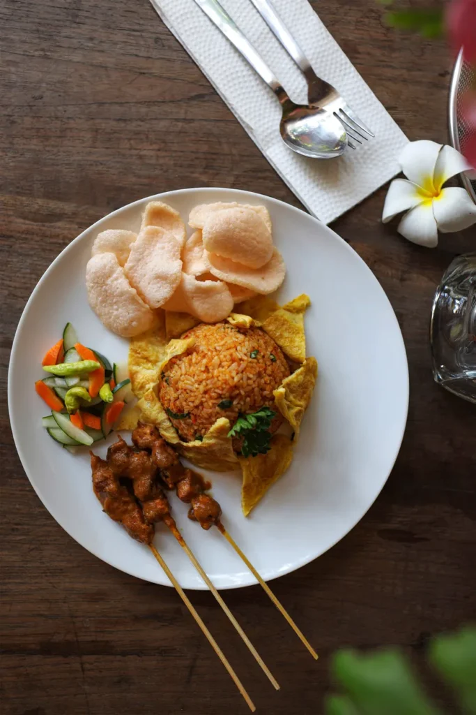 Indonesian Nasi Goreng with chicken satay and prawn crackers served on a wooden table.