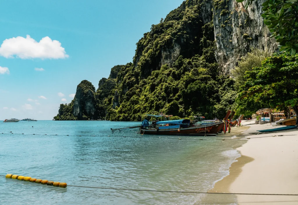 Longtail boats resting on a serene beach at Ko Panyi, Phang Nga, Thailand with lush cliffs.