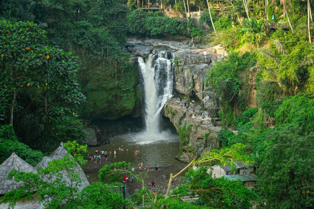 Lush jungle surrounds Tegenungan Waterfall in Bali, with tourists enjoying the scenic view.