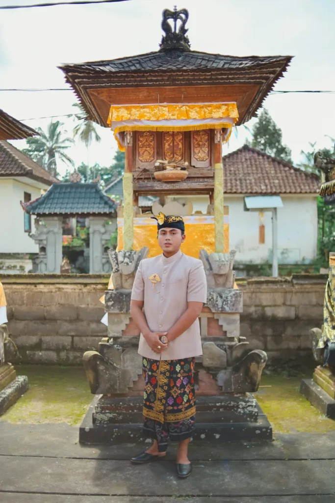 Man in traditional Balinese attire standing in front of temple structure.