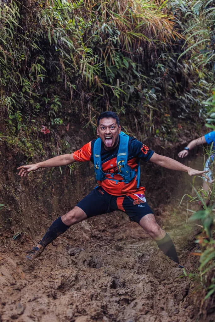 Man joyfully navigating a challenging muddy trail in a vibrant forest setting during daytime.