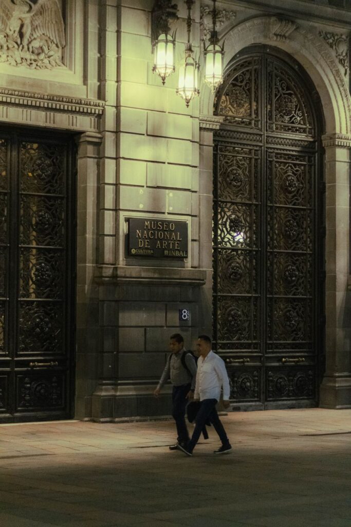 Men walking by the Museo Nacional de Arte entrance in Mexico City at night.