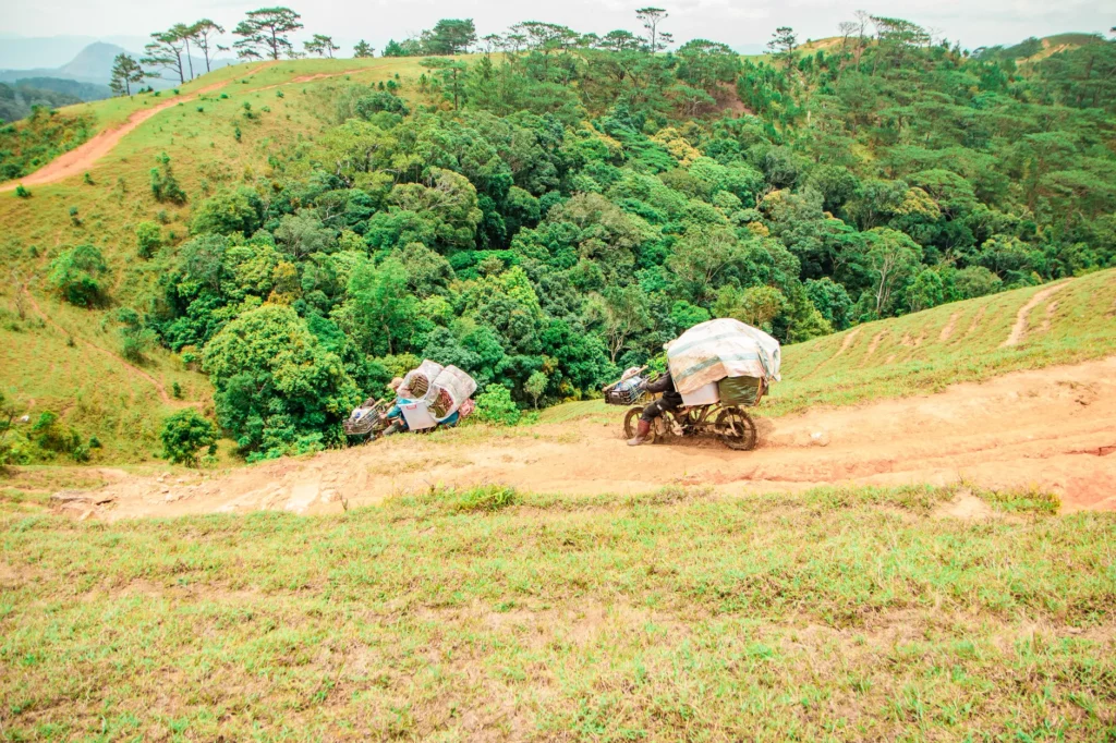 Motorbikes navigate a steep, dirt path through lush hills in Lâm Đồng, Vietnam.