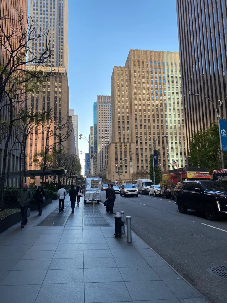 New York City street scene featuring tall skyscrapers and people walking on the sidewalk.