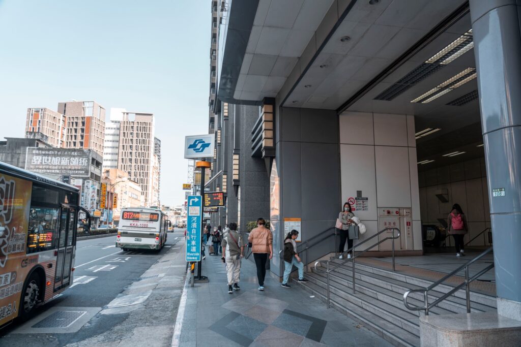 People entering a modern urban train station with bus and skyscrapers nearby.
