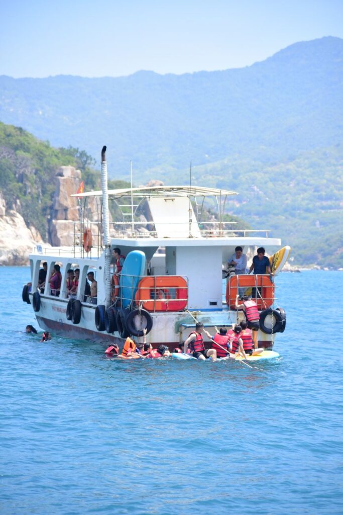 People snorkeling near a boat with scenic coastal views in sunny weather.