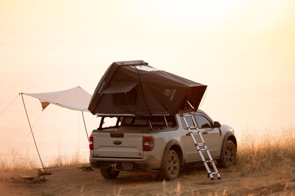 Pickup truck with rooftop tent in scenic outdoor camping setup at sunset.
