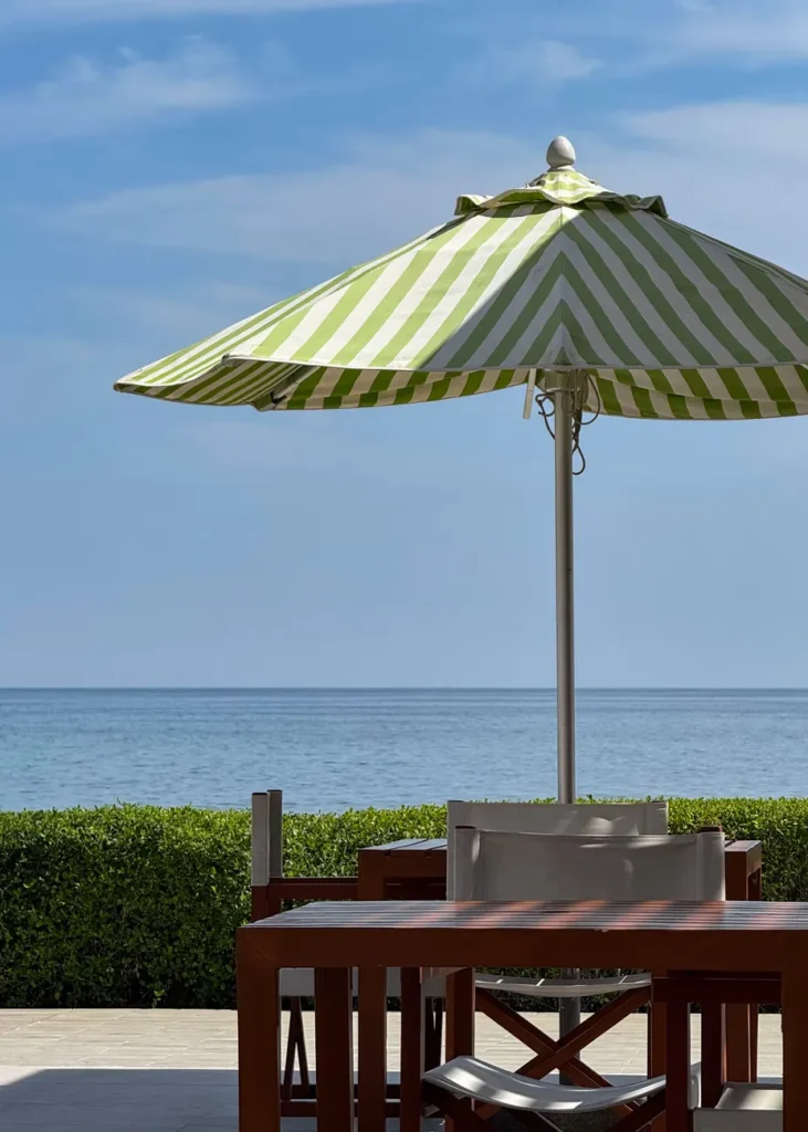 Relaxing beachside terrace featuring a green striped parasol and ocean view.