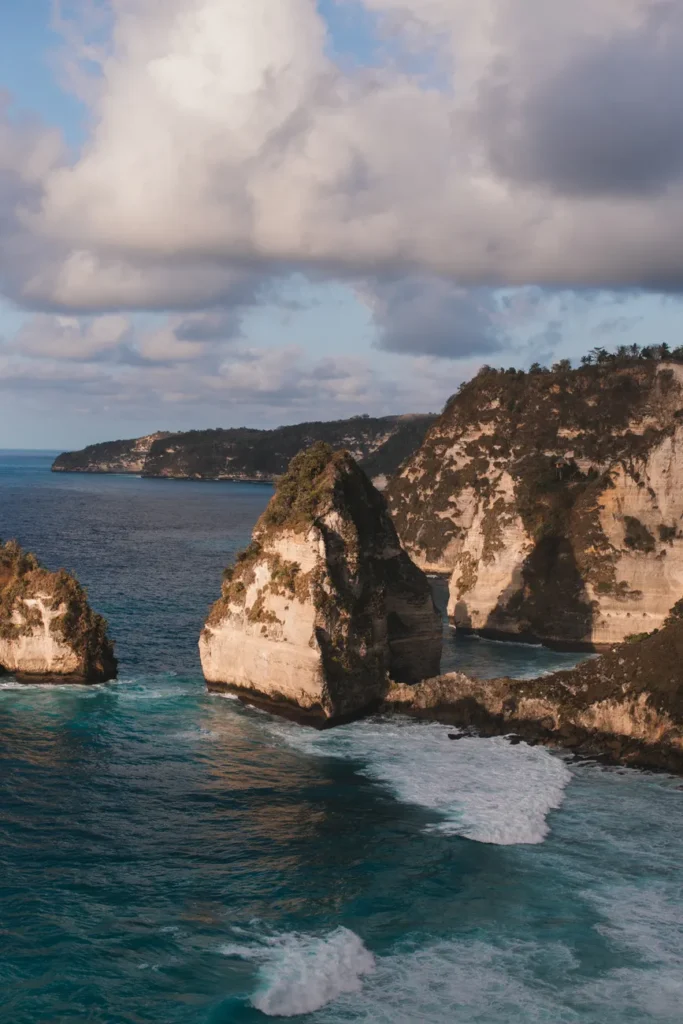 Rough stony cliffs covered with moss and washed by turquoise water of foamy ocean under cloudy sky