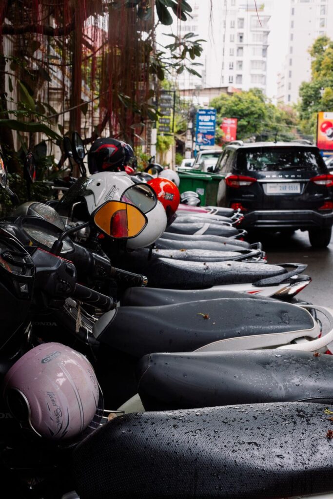 Row of parked motor scooters and cars on a wet urban street after rain.