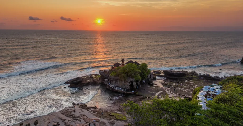 Bali en couple : visiter les temples sans vous faire aspirer par la foule (guide concret) Scenic sunset view over Tanah Lot Temple surrounded by ocean and lush greenery in Bali.