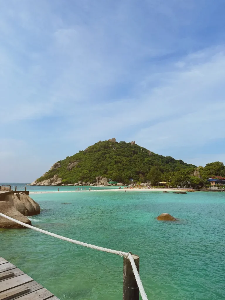 Scenic tropical beach with turquoise waters and lush greenery under a bright blue sky.