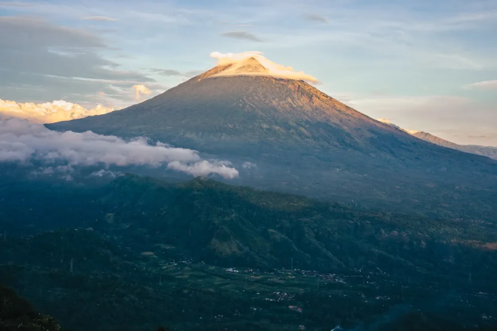 Scenic view of Mount Agung basking in warm sunrise light, surrounded by clouds in Bali, Indonesia.