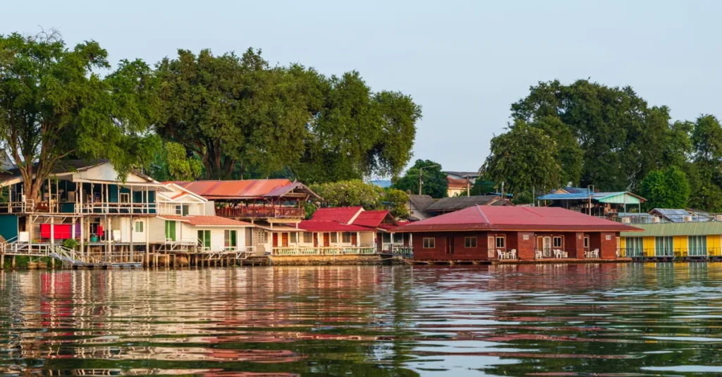 Tanjung Puting en couple : voir les orangs-outans, dormir sur un Klotok et éviter les pièges Scenic view of riverside houses in Kanchanaburi, Thailand, reflecting tranquil waters at sunset.