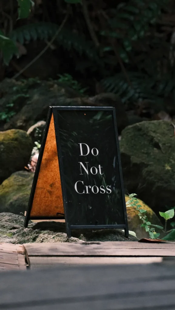 Sign reading 'Do Not Cross' amidst rocks and foliage in a natural setting.