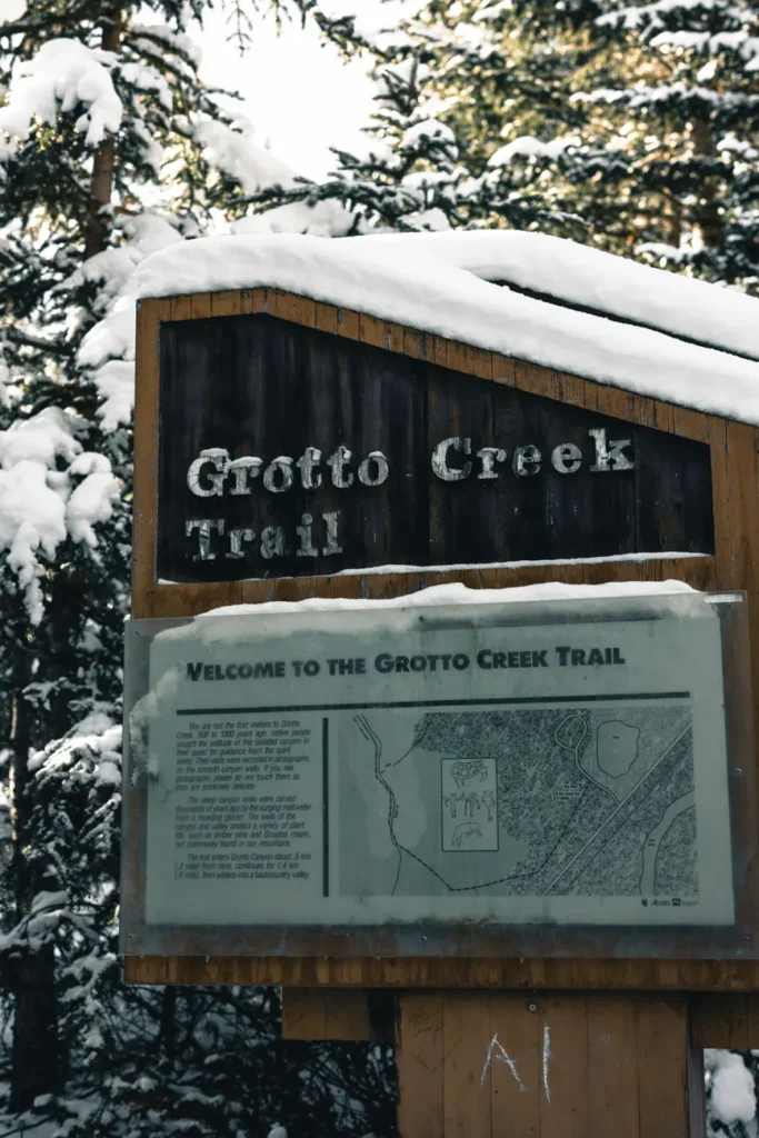 Snow-covered Grotto Creek Trail sign and map welcoming hikers in winter.
