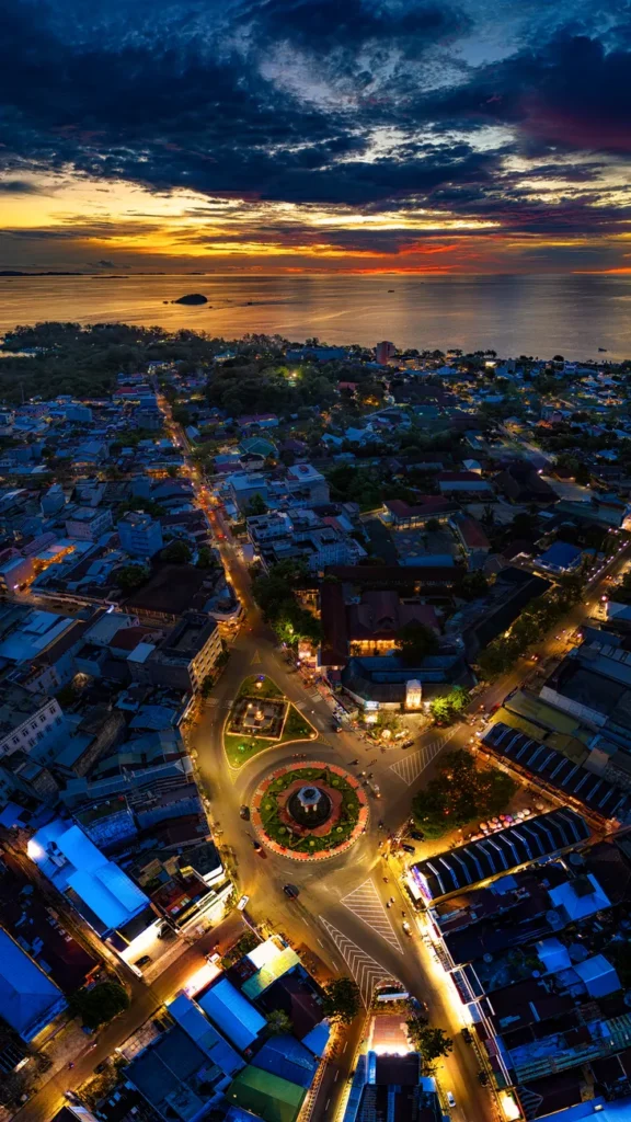 Stunning aerial shot of Tanjung Pandan cityscape during a vibrant sunset with city lights and ocean view.