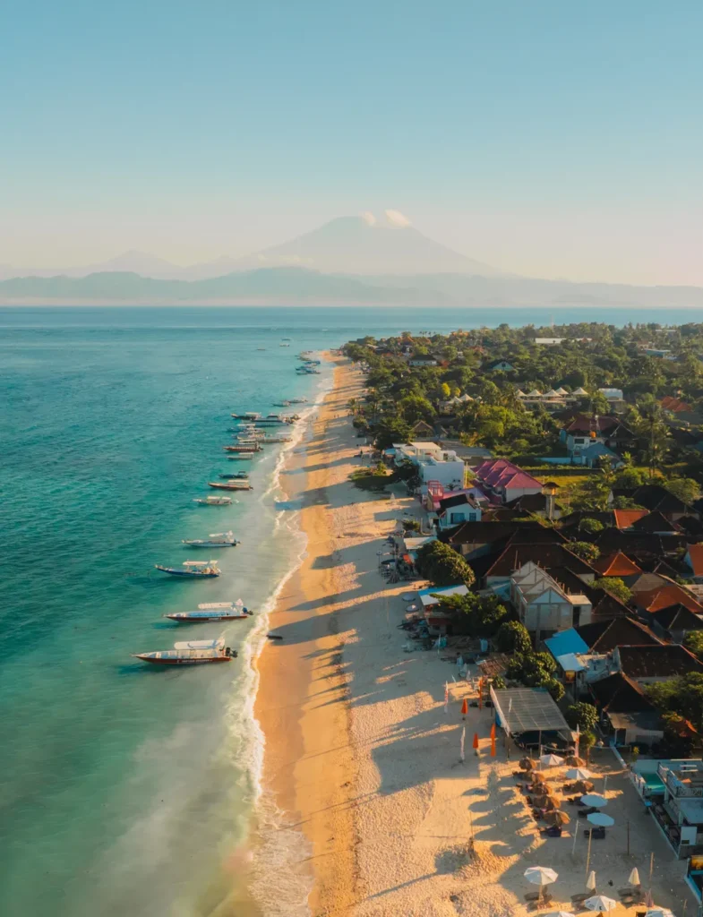 Stunning aerial view of Bali's coastline with Mount Agung in the background at sunrise.