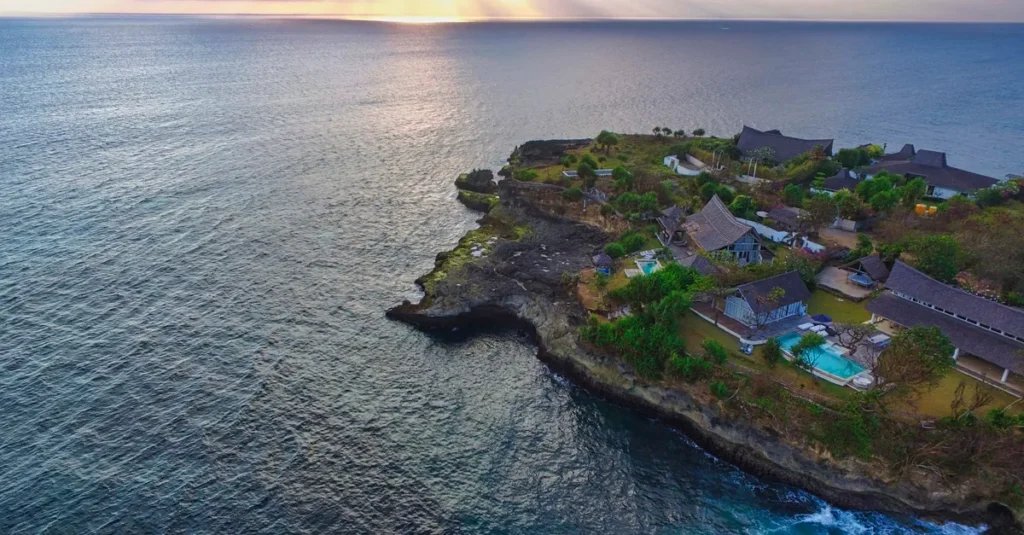 Crystal Bay à Nusa Penida en couple : le sunset qui fait le job (sans se compliquer la vie) Stunning aerial view of Nusa Penida's coastline at sunset, featuring villas and lush greenery.