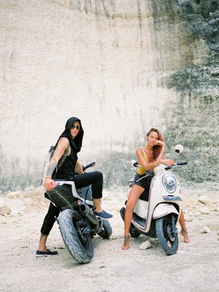 Stylish couple posing with scooters on a dirt road in Bali, Indonesia for a travel adventure.