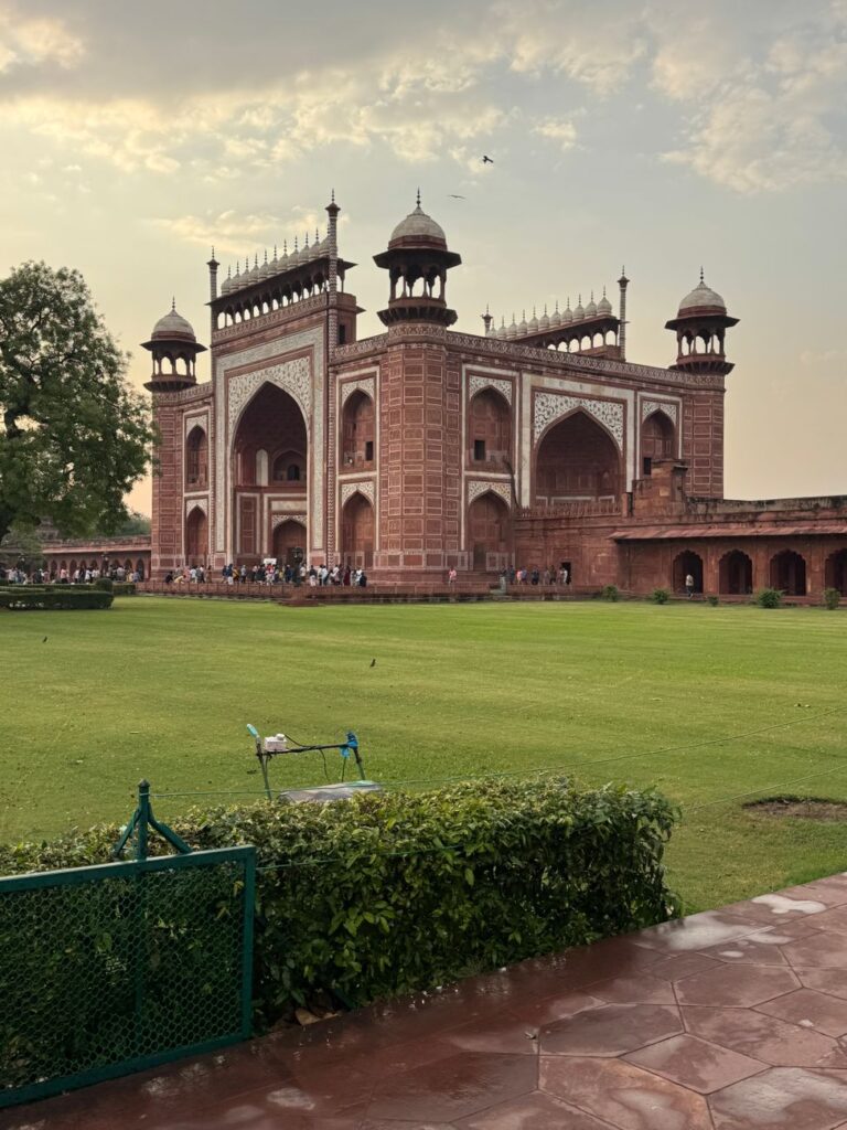 The grand entrance gate of the Taj Mahal, showcasing Mughal architecture with lush green lawns.