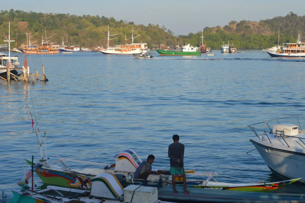 Two men on a colorful fishing boat in a vibrant harbor with boats, capturing serene marine life at dusk.